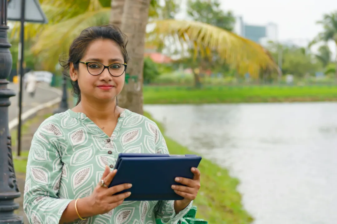 A young professional holding a tablet outdoors, smiling at the camera
