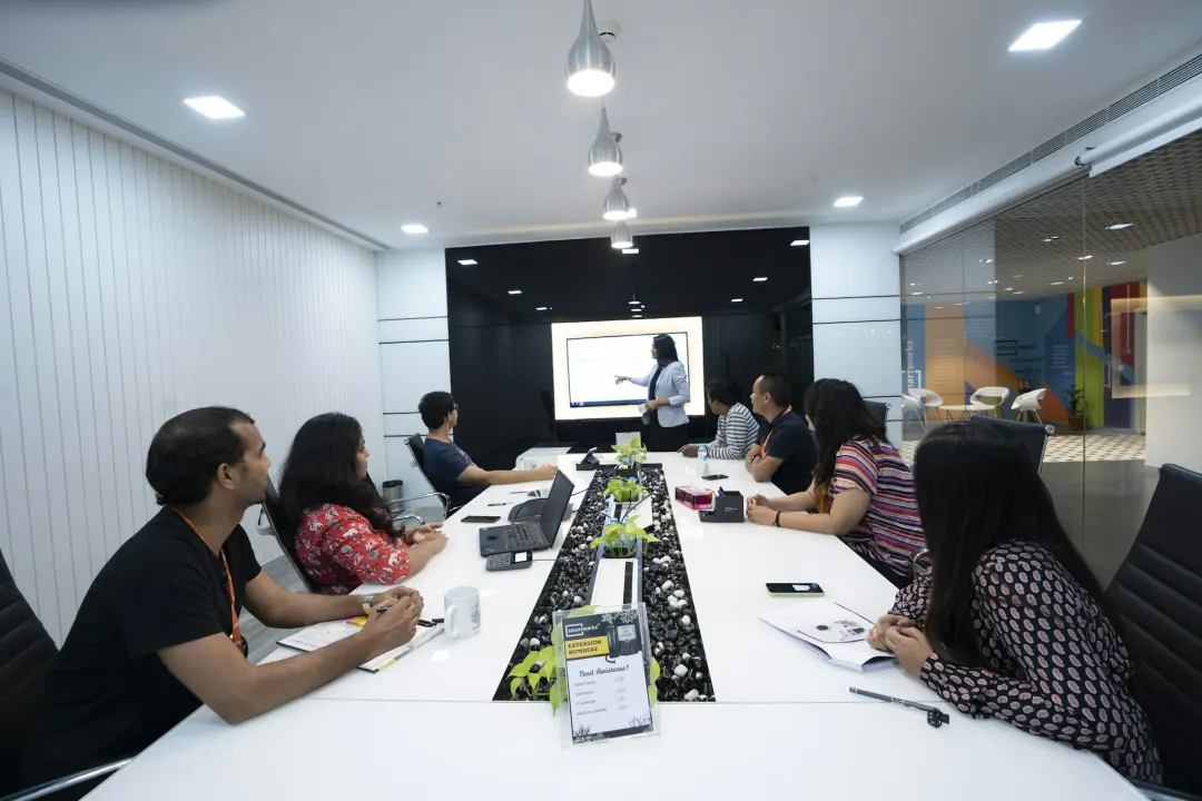 A team around a long table watching a colleague present on a screen